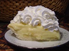 a piece of pie with whipped cream on top sits on a plate in front of a wicker basket