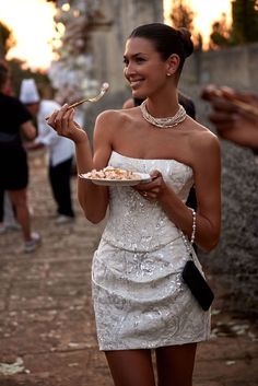 a woman in a white dress holding a plate with food on it