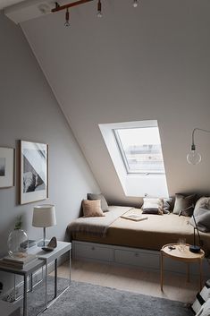 a bed sitting under a window in a bedroom next to a table and lamp on top of a rug