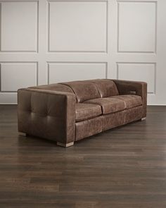 a brown couch sitting on top of a hard wood floor next to a white wall