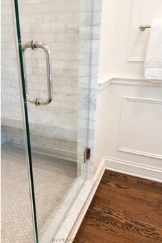 a glass shower door in a bathroom with wood floors and white tile on the walls