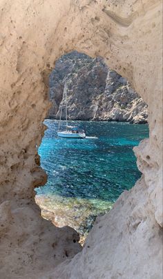 a boat in the water seen through a hole in a rock wall with blue water