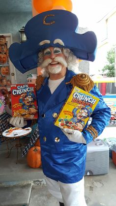 a man dressed up in a blue suit and hat holding a cereal box while standing next to a table