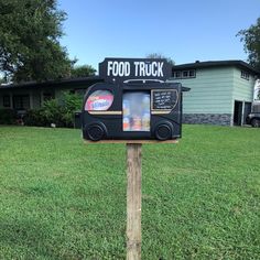 a food truck sign on top of a wooden post in front of a green house