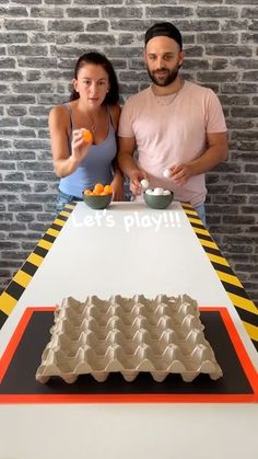 a man and woman standing next to a table with an egg carton on it