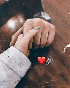 two hands holding each other on top of a wooden table next to a red heart