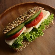 a sandwich with lettuce, tomato and cheese on it sitting on a wooden plate