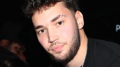 a close up of a person with a beard wearing a black shirt and chain around his neck