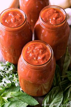 four jars filled with tomato sauce sitting on top of green leaves and vegetables next to each other