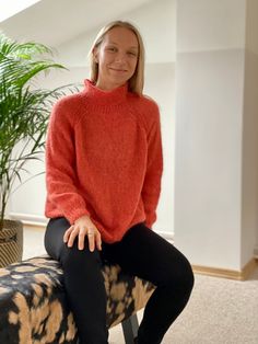 a woman in an orange sweater is sitting on a black and white chair next to a potted plant