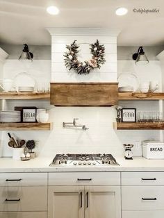 a white kitchen with open shelving and wooden shelves on the wall above the stove