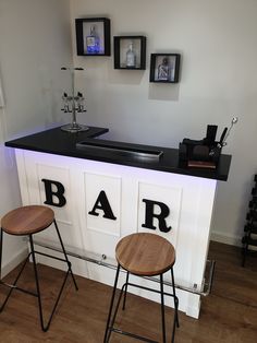 two bar stools sitting in front of a white counter with black letters on it