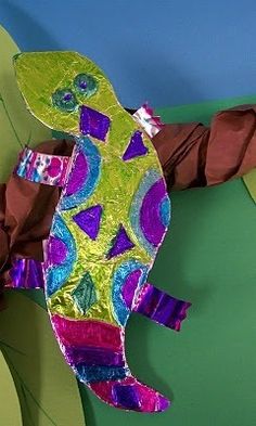 a paper mache of a gecko on a leafy green background with purple and blue accents