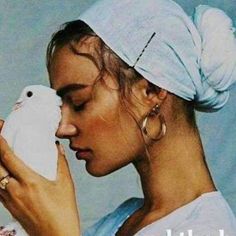 a woman holding a white bird in her right hand and wearing a head scarf on top of her head