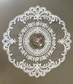 a white doily with pink flowers and leaves in the center on a gray background