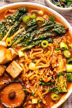 a bowl filled with noodles, vegetables and tofu on top of a newspaper next to two bowls of broccoli