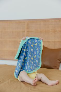 a baby laying on top of a bed under a blue and yellow blanket with fish print