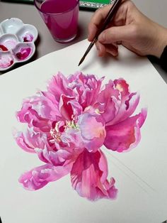 a person is holding a paintbrush and drawing flowers on paper with watercolors