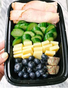 a person holding a tray with different types of fruits and vegetables in it on a table