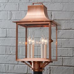 a lantern with five lit candles in front of a brick wall