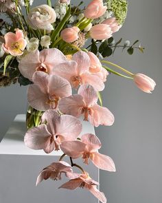 a vase filled with pink and white flowers on top of a table next to a wall