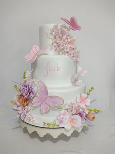 a three tiered white cake with pink flowers and butterflies on the top, decorated with name yoke