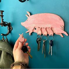 a person is holding keys to a pig shaped key holder on a blue wall with other items