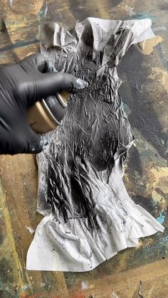 a person in black gloves is painting a piece of paper with silver foil on it