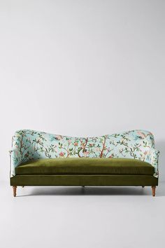 an upholstered green couch with birds and flowers on the back, in front of a white wall