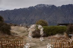 an outdoor wedding setup with chairs and flowers on the aisle, in front of mountains