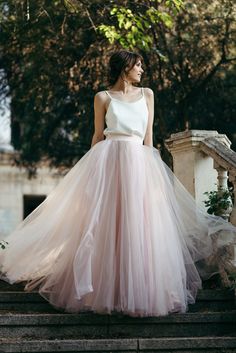 a woman standing on some steps wearing a pink and white dress with sheer tulle