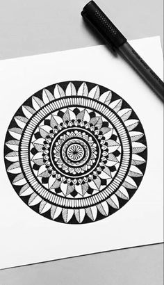 a black and white drawing of a circular design on paper next to a marker pen