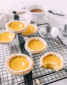 four pies sitting on top of a cooling rack next to cups and saucers