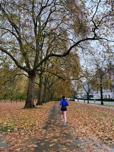 a person running down a leaf covered path in the middle of a tree lined park