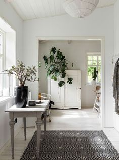 a living room with white walls and flooring, plants on the table in vases