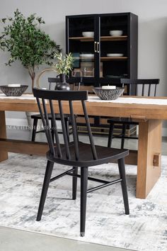 a dining room table with black chairs and plates on top of it, in front of a bookcase