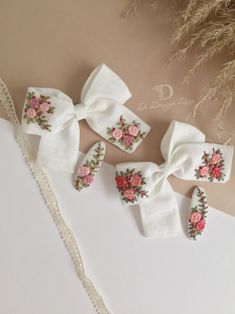 four white bows with pink flowers on them sitting on top of a table next to a lace doily