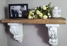 two white vases with flowers are sitting on a shelf next to a framed photo