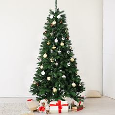 a small christmas tree with presents under it on the floor next to a white wall