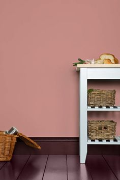 a shelf with baskets and bread on it in front of a pink wall, against a wooden floor