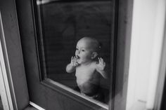 a baby is looking out the window and waving his hands at someone in the mirror