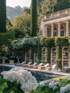 an outdoor pool surrounded by greenery and white hydrangeas in front of a large house