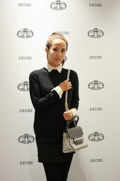 a woman holding a purse in front of a white wall with the word deucee on it