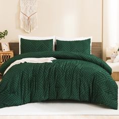 a bed with green comforter and pillows in a room next to a plant on the floor