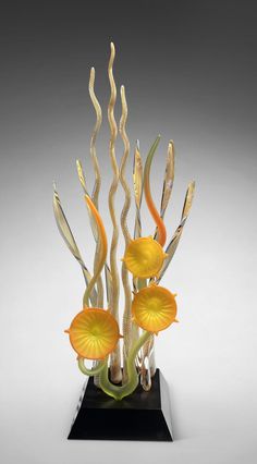 a glass sculpture with yellow flowers and green leaves on a black base in front of a gray background