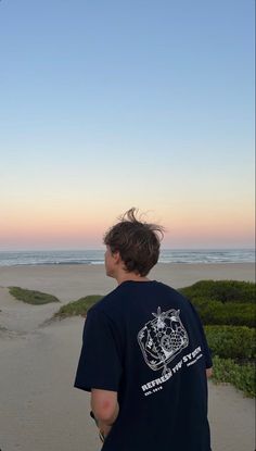 a man standing on top of a sandy beach next to the ocean under a blue sky