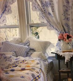 a bed with white and blue sheets in front of a window next to a small table