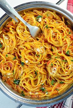 a pot filled with pasta and sauce on top of a towel next to a fork