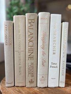 four books are lined up on a wooden table in front of a potted plant