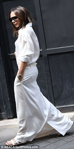 the woman is walking down the street wearing white clothing and sunglasses, with her hair pulled back